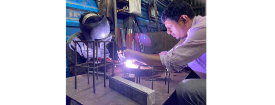 In the workshop overseeing the welding process, while trying not to get in the way of all the workers there.